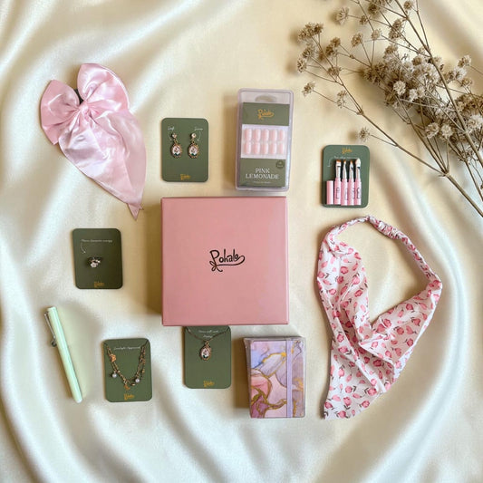 Collection of beauty products including a pink hair mask, earrings, pencil, a bow, makeup brushes, press on nails, necklace, bracelet, diary branded with pohalo 