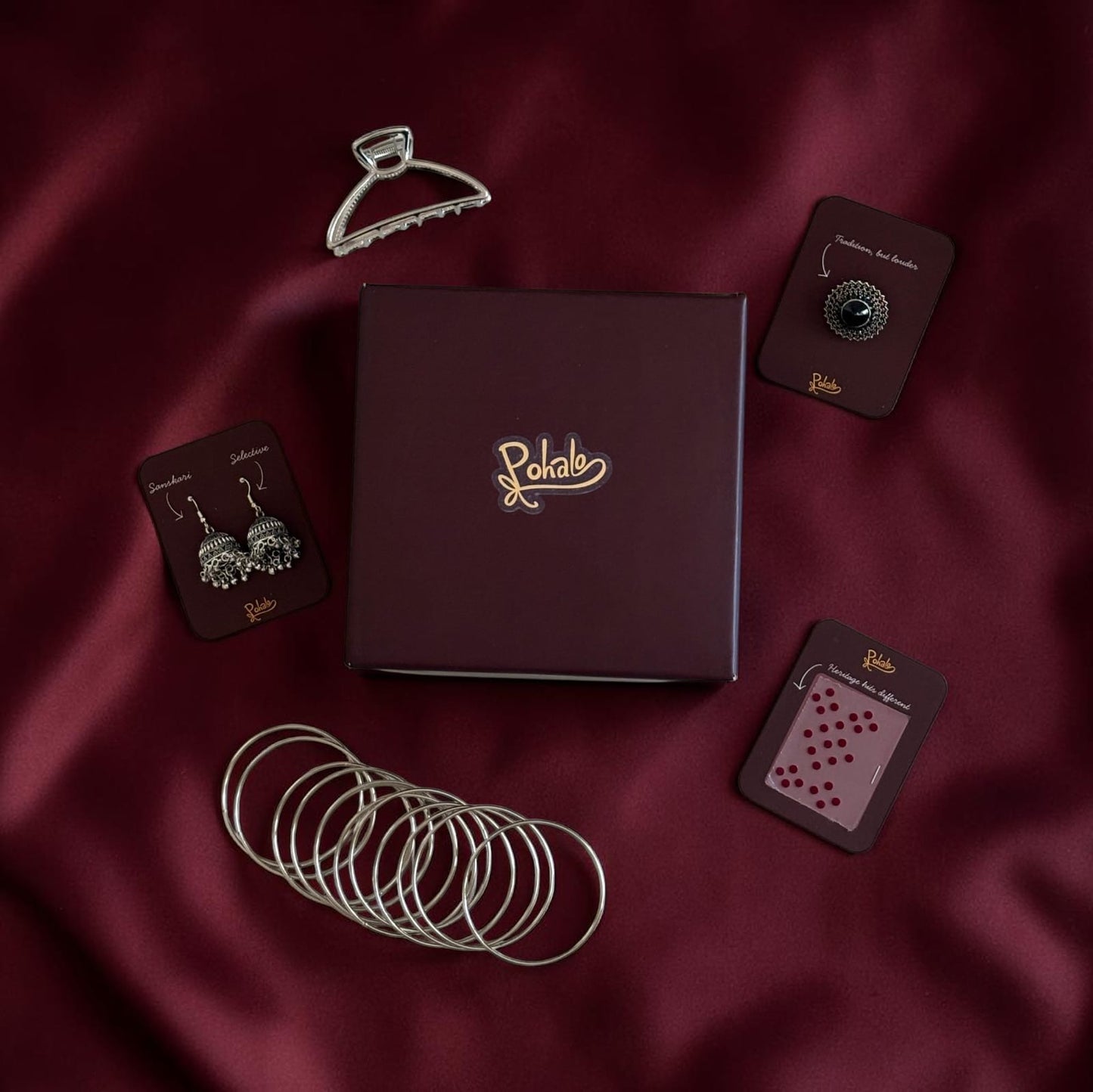 Jewelry set with bangles, earrings, and a box on a maroon fabric background