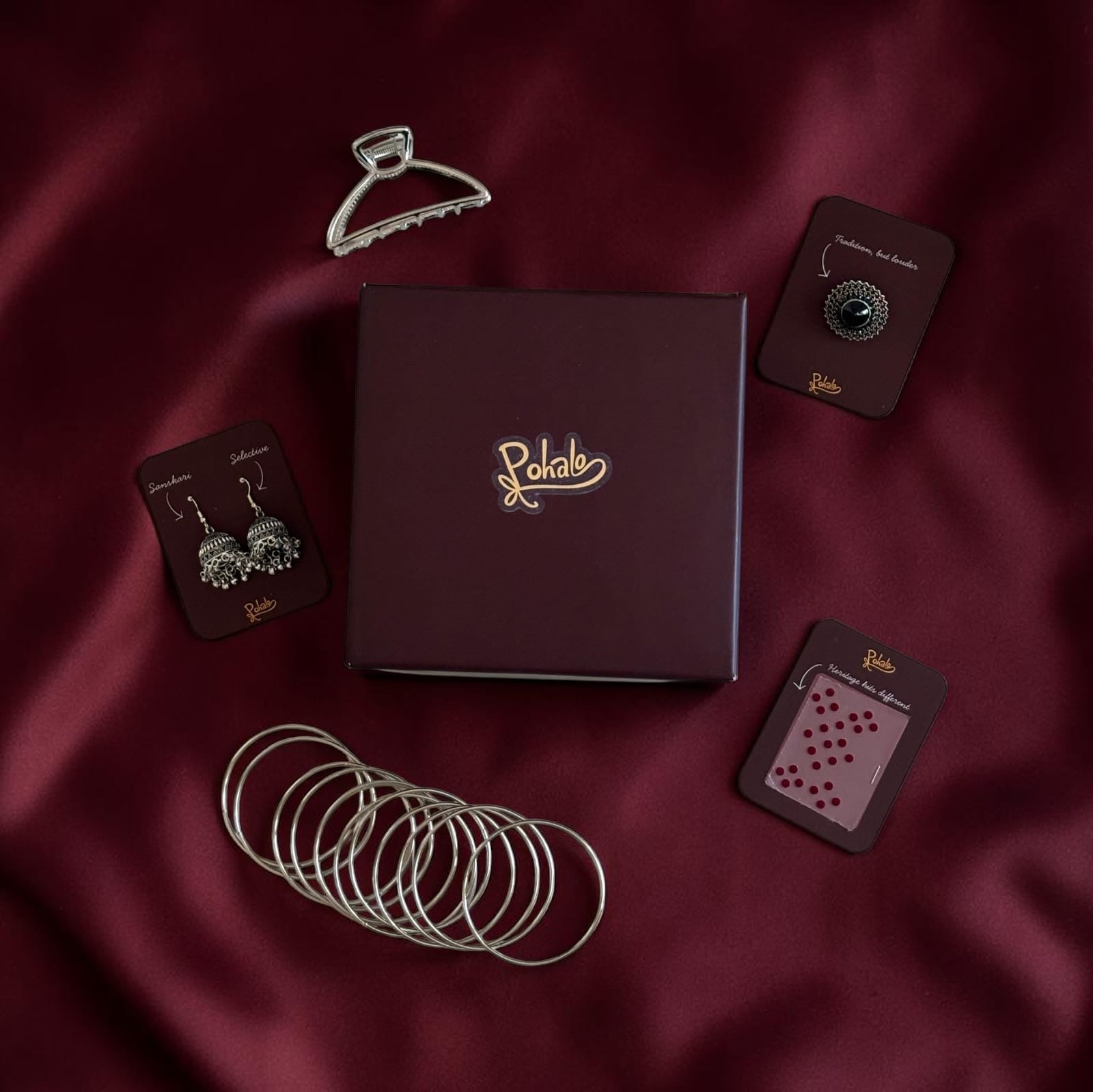Jewelry set with bangles, earrings, and a box on a maroon fabric background