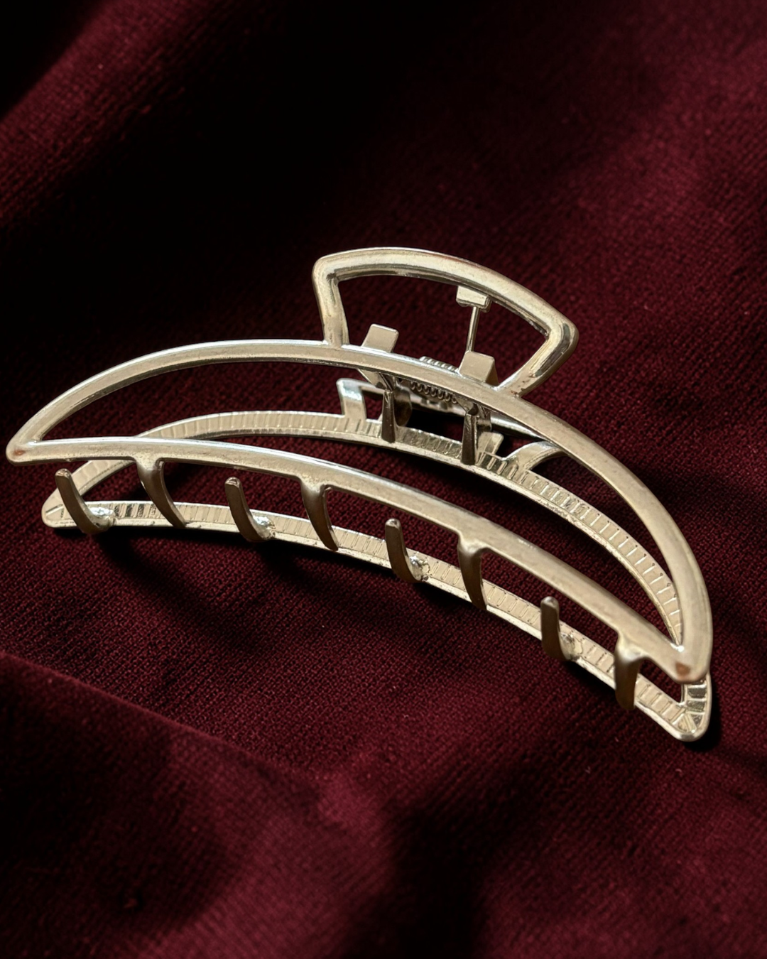 Silver hair clip on a dark maroon fabric background