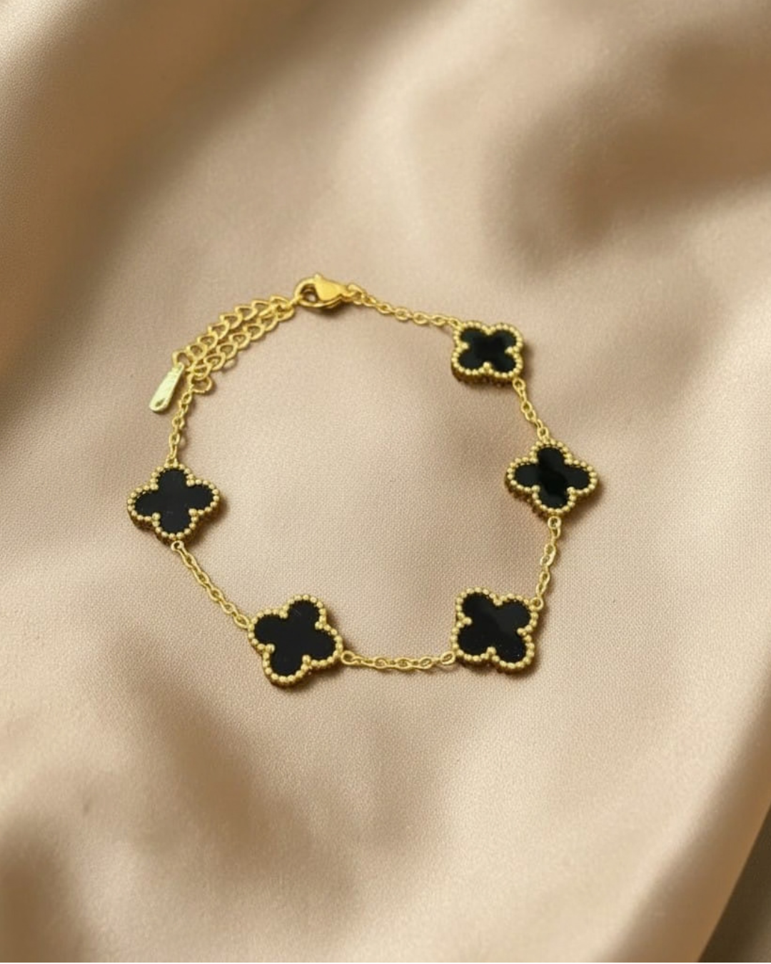 Gold bracelet with black clover-shaped charms on a beige fabric background