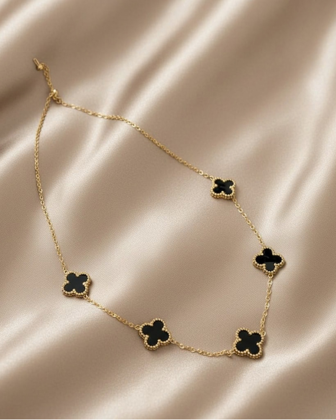 Gold necklace with black clover-shaped pendants on a beige fabric background