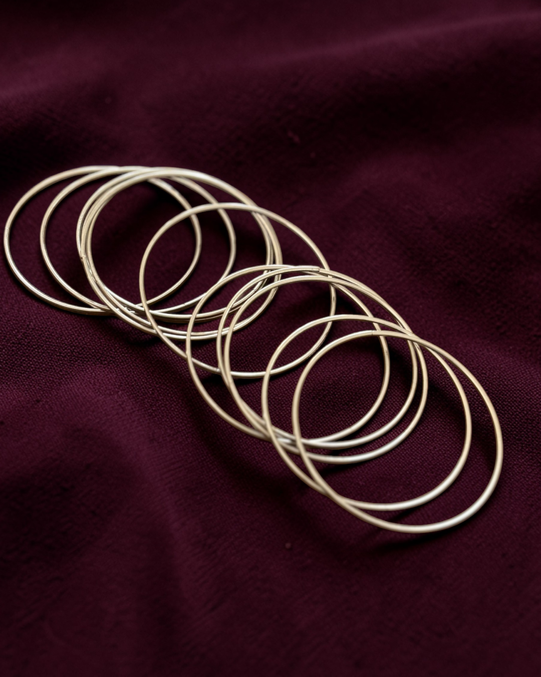 Set of silver bangles on a dark maroon fabric background