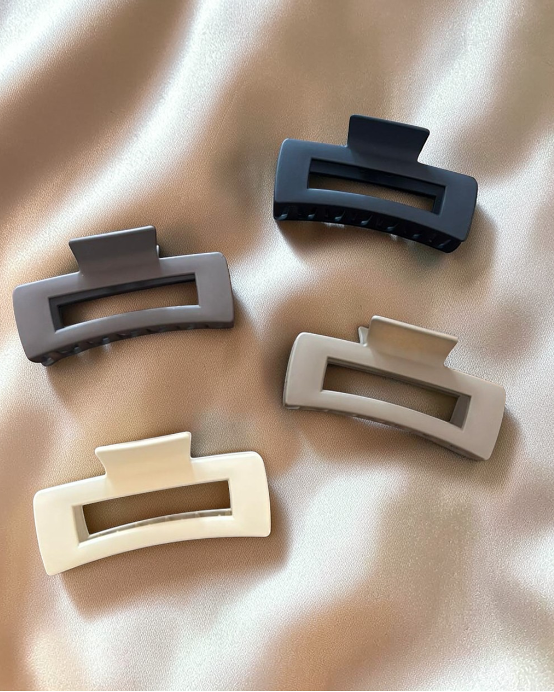 Four hair clips in black, gray, beige, and white on a beige fabric background