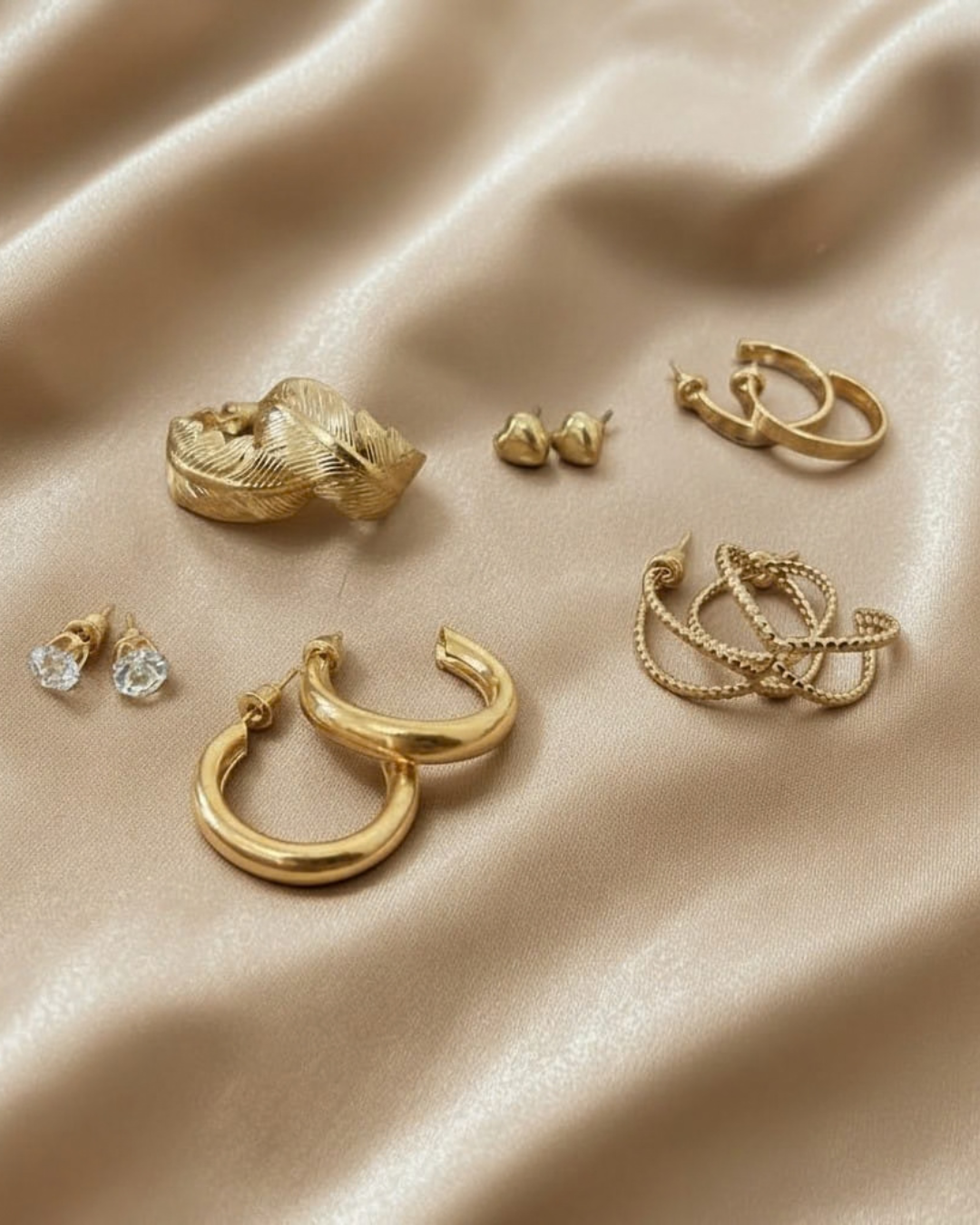 Collection of gold earrings on a beige fabric background