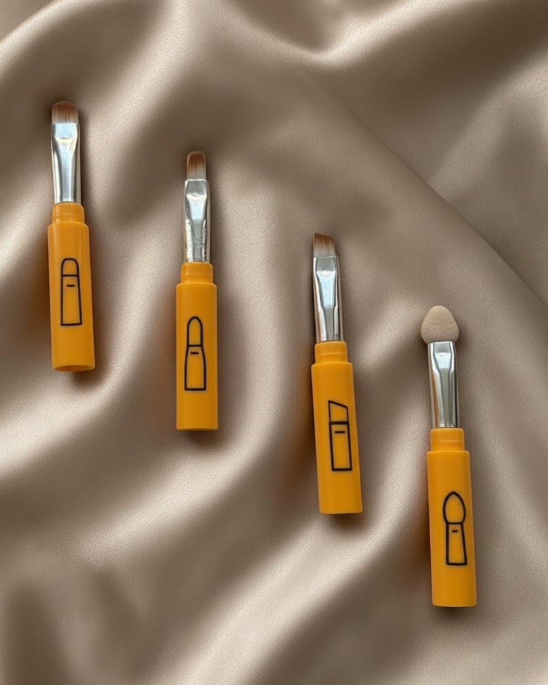 Four makeup bushes poratable small tools with yellow handles and metallic heads on a beige fabric background