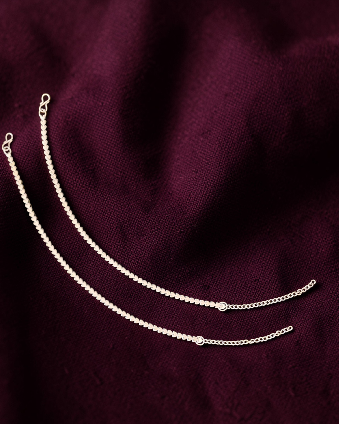 Two silver chains on a dark maroon fabric background