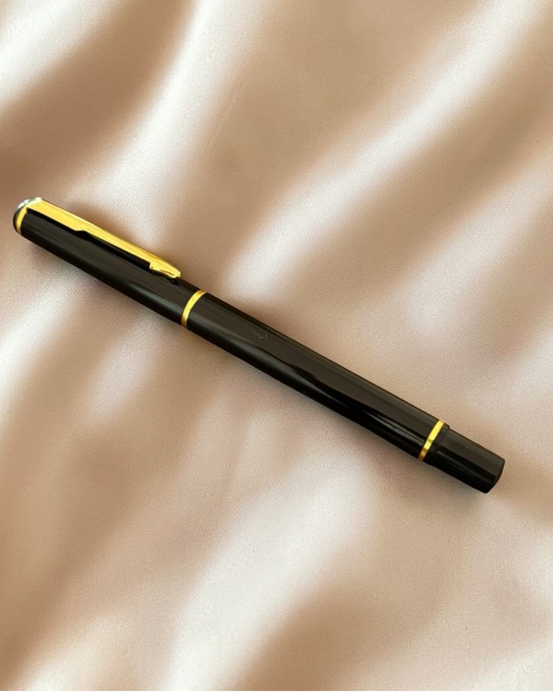 Black pen with gold accents on a beige fabric background