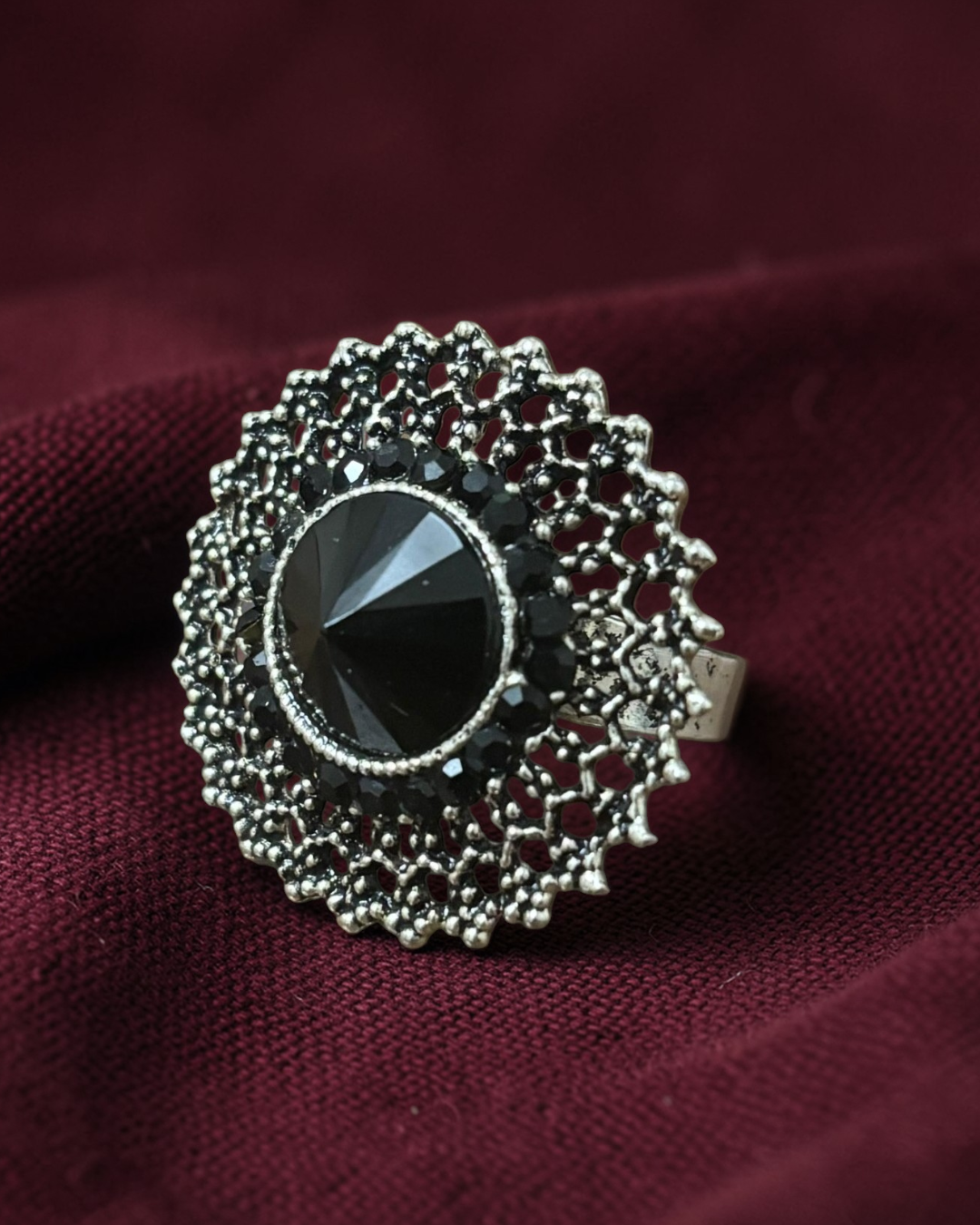 Silver ring with a black gemstone on a maroon fabric background
