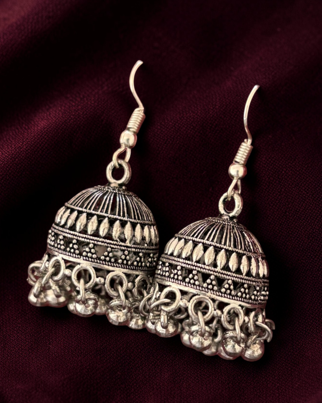 Pair of silver earrings on a dark Maroon background