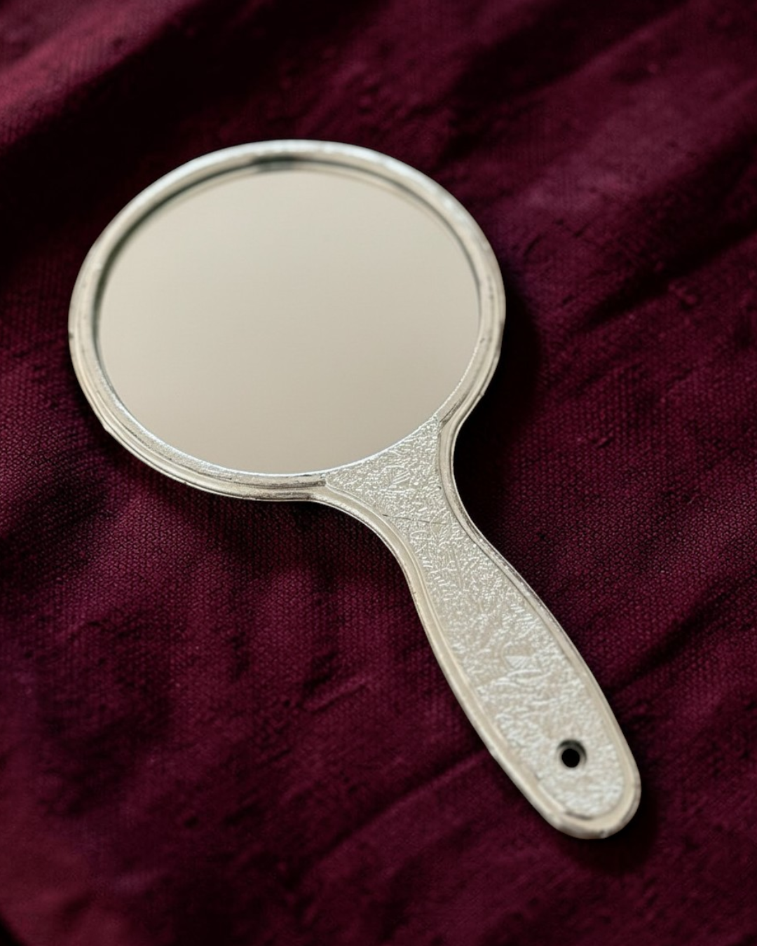 Handheld mirror with decorative handle on a maroon fabric background